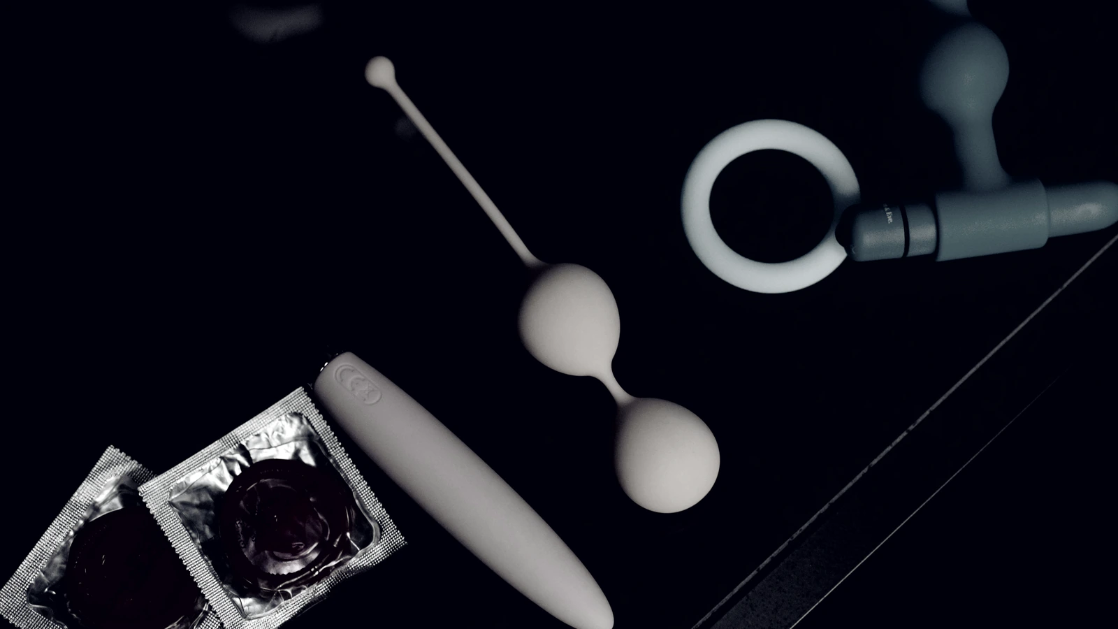 Sobre fondo negro: un anillo, dos preservativos en su envoltorio y varias piezas de silicona
